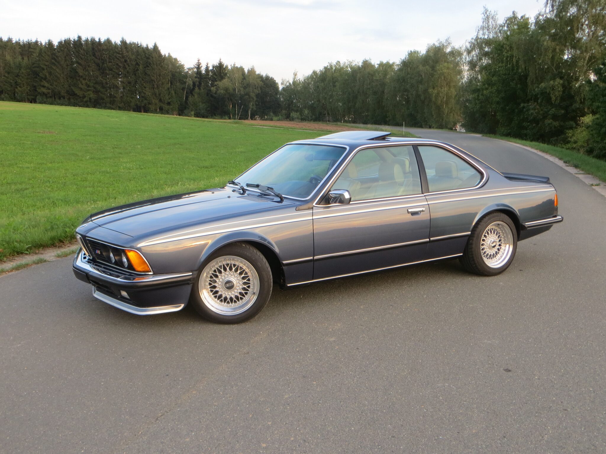 Grauer BMW E24 auf einer Landstraße im Abendlicht