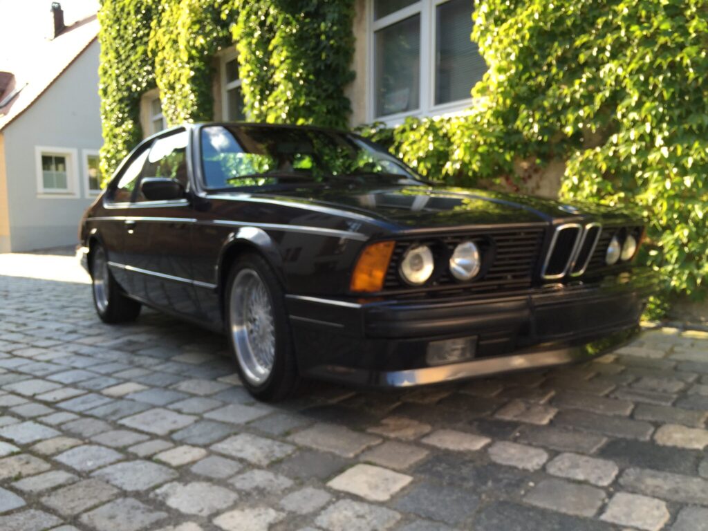 Schwarzer BMW E24 vor einer efeubewachsenen Fassade